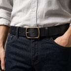 Black full-grain men's leather belt with brass buckle, worn with jeans